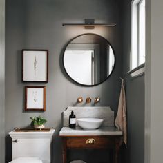 a white toilet sitting next to a bathroom sink under a round mirror on a wall