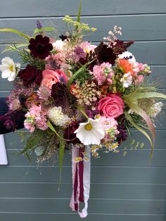 a bridal bouquet with pink, red and white flowers in front of a blue wall