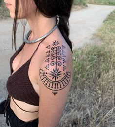 a woman with a black and white tattoo on her shoulder standing next to a dirt road