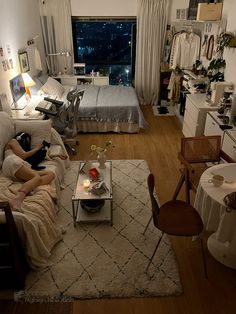 a living room filled with furniture and a bed next to a large window at night