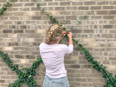 a woman standing in front of a brick wall with ivy growing on it's sides