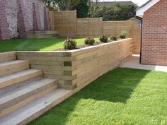 a wooden planter sitting on the side of a lush green lawn next to a brick building