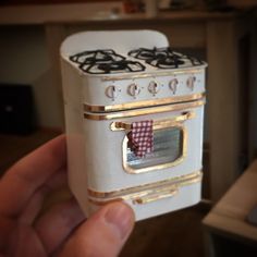 a hand holding up a miniature stove in the shape of a house or kitchen oven