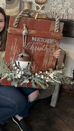 a woman sitting on the floor holding up a wooden sign that says merry christmas and decorated with greenery