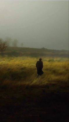 a lone man standing in the middle of a grassy field on a foggy day