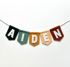 the word aiden spelled with felt letters on a white background hanging from a string