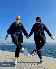 two people are walking on the pier holding hands and wearing black clothing with white socks