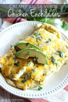 an enchilada on a white plate with avocado and cilantro