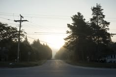 the sun is setting on an empty street with power lines in the foreground and telephone poles to the right