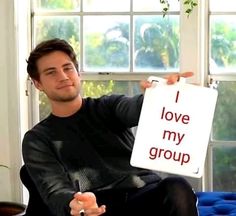 a man sitting in a chair holding up a sign that says i love my group