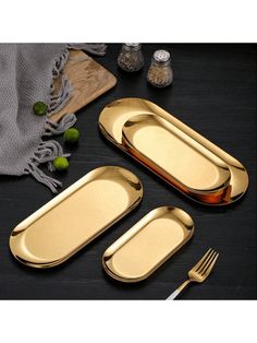 three pieces of goldware on a black table with silverware and utensils