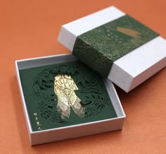 an open box with a gold feather brooch sitting on top of it's side