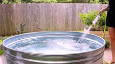 a person is using a hose to clean the water in a large metal tub outside