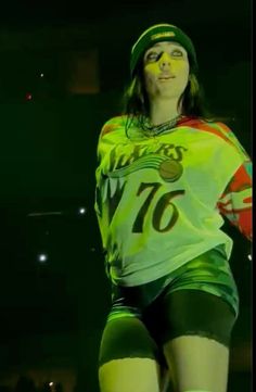 a woman in green shorts and yellow shirt with her hands behind her back as she stands on a stage