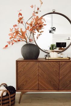 a round mirror sitting on top of a wooden dresser next to a vase filled with flowers