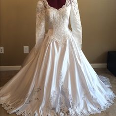 a white wedding dress with long sleeves and lace on the skirt is displayed in front of a mannequin