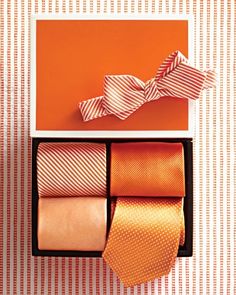 an orange tie and three matching ties in a box on a striped wallpaper background