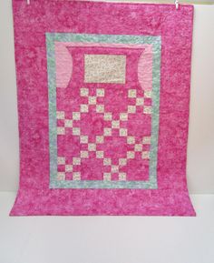 a pink quilt hanging on a white wall