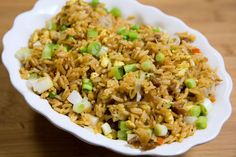 a white bowl filled with rice and vegetables on top of a wooden table next to a fork