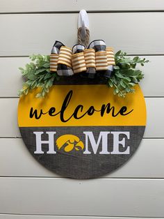 a welcome home sign hanging on the side of a building with shoes and greenery