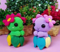 two crocheted stuffed animals sitting next to each other in front of flowers and plants