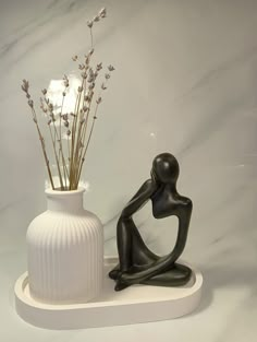 a white vase with some flowers in it and a black figure sitting next to it