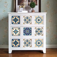 a white dresser with blue and yellow tiles on the drawers in front of a painting