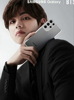 a man in a suit holding up a samsung galaxy note 10 pro with its camera