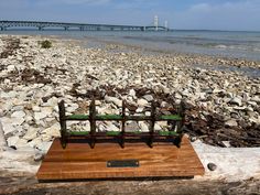 a wooden bench sitting on top of a rocky beach next to the ocean with a bridge in the background