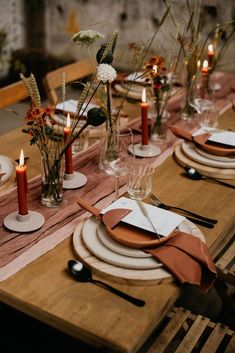 a wooden table topped with plates and glasses filled with flowers, candles and napkins