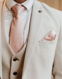 a man in a white suit with a pink tie and pocket square on his lapel