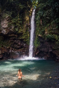 a woman standing in the water near a waterfall