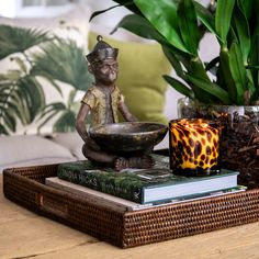 a wooden table topped with books and a statue on top of each other next to a potted plant