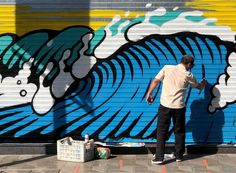 a man is painting a mural on the side of a building in front of a garage door