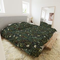 there is a bed with a green floral comforter on it and a mirror in the corner