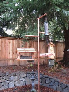 a bird feeder in the shape of a tree with birds on it and a wooden fence behind it