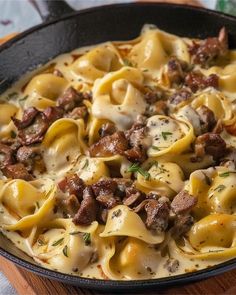 a skillet filled with pasta, meat and cheese on top of a wooden cutting board