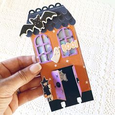 a hand holding up a halloween card with a house and ghost on the front door