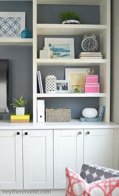 a living room with white bookcases and various items on top of the bookshelves