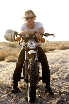 a man sitting on top of a motorcycle in the desert