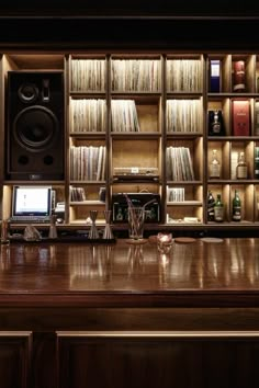 a large wooden desk in front of a bookshelf with speakers and other items on it