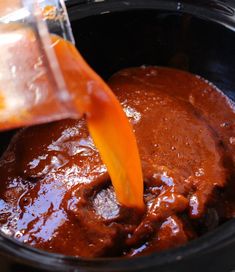 someone pouring sauce into a slow cooker with an orange spatula in the bowl