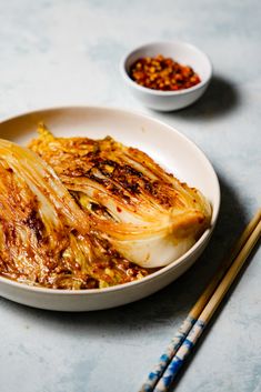 a white bowl filled with food next to chopsticks on a blue counter top