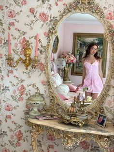 a woman standing in front of a mirror next to a table with candles on it