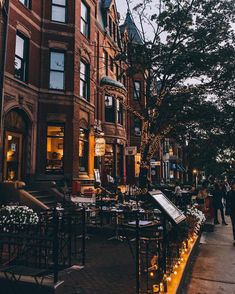 people are walking down the sidewalk in front of an old brick building with christmas lights on it