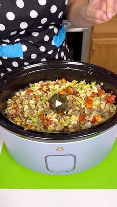 a woman in polka dot shirt standing next to a crock pot filled with food