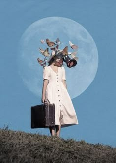 a woman standing on top of a hill holding a suitcase and butterflies above her head