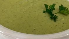 a white bowl filled with broccoli soup and garnished with parsley