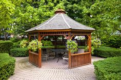 a wooden gazebo sitting in the middle of a garden surrounded by bushes and trees