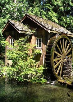 an old water wheel is next to a small cabin in the woods near a stream